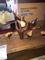 Wooden bird sculpture featuring a branch base with five carved birds displayed on a wood surface in a cluttered room.