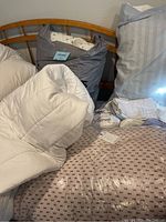 White quilted mattress pad, gray bag packaging, striped pillow, and some pillowcases visible.