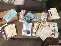 Overview of multiple cookbooks laid out on table with some stacked, showing varied covers and binding types.