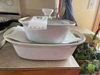 Two white Corning Ware casserole dishes, smaller one on top of larger one with glass lid and integrated handles.
