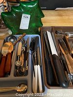 Full view of light blue plastic cutlery tray filled with various stainless steel flatware, knives, and kitchen utensils alongside green Christmas tree shaped tray.