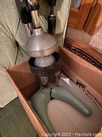 Juicer showing metallic dome and strainer inside a cardboard box with green handle and black parts.