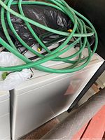 Side view of the white Kenmore washing machine with green hoses coiled on top and part of a black plastic sheet nearby.