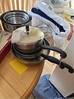Four Farberware pans and four stainless steel nesting bowls placed on a wooden table with some towels in the background.