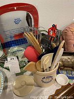 Photo showing assortment of kitchen utensils in ceramic crock with Old Alaska Sourdough branding alongside green glass bowl.