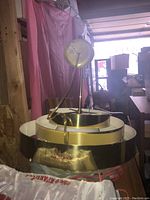 Light fixture held up to show underside and rings arrangement, polished brass finish reflecting surrounding environment.