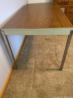 Photo of a metal market table assembled with wood-patterned laminate top, showing metal legs and beige skirt/frame.