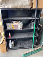Front view of black metal shelving unit with items on shelves for scale only, showing three shelves and visible dust and dirt.