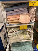 Plastic shelving rack holding folded towels and bed linens on three shelves