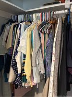 Hanging closet with women's tops, shirts, sweaters, and vests in various colors and patterns on hangers.