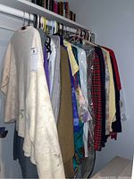 Full view of hanging clothes on a metal rod, showing a range of women's sweaters, tops, shirts, skirts, and dresses in multiple colors and patterns.