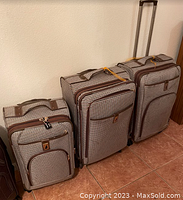 Three London Fog luggage pieces stacked against wall, brown and beige houndstooth pattern, showing sizes and features like wheels and handles