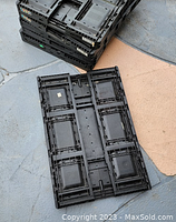 Stack of black folded folding pallet containers seen from the top, showing grid and vented design.