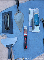 Full set of six plaster construction tools displayed on blue surface including floats, trowels, and putty knife