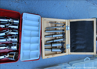 Opened wooden box with 8 barrel plug reamers of varying sizes and a separate red plastic case with socket wrench attachments or drill bits.
