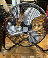 Front view of metal drum fan with three blades and black protective grille with stand frame.
