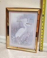 Framed fine art painting showing two white egrets with floral and natural background, gold frame with beveled edges, photo includes measuring tape indicating size around 12 inches tall.
