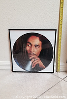 Photo of the framed Bob Marley record print showing the image and size reference with a tape measure.