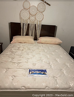 Photo of full size bed with mattress, pillows, and headboard against white wall with wall decor