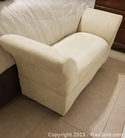 Side angle view showing cream velvet fabric and padded armrest on a mini chaise lounge next to bed.