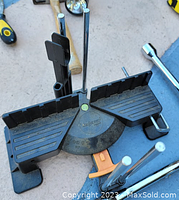 Photo of miter saw holder with bubble level, metal rods, hammer, and screwdriver on a blue surface.