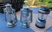 Three lanterns on a table: two old metal hurricane lamps and one modern LED lantern