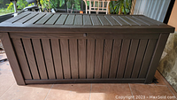 Front and top view of large dark brown outdoor storage box with slatted design and hinged lid.