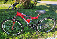 Full side view of red Next Powerclimber dual suspension mountain bike with knobby tires and black seat on grassy ground.