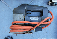 Black & Decker professional electric sander with orange power cord coiled around it, laying on a flat surface.
