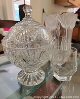 Photo showing a vintage crystal lidded bowl on a pedestal, two tall etched vases, and two small clear glass cups on a glass table.