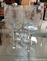Four vintage crystal wine glasses with etched grape and leaf pattern on the bowl, placed on a reflective surface.