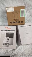 Photo showing boxed Pet Fountain, Rollwish Smart Pet Feeder, and Automatic Pet Feeder in their original packaging