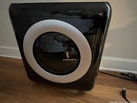 Front view of the black Coway air purifier showing the circular transparent window with the white ring and Coway branding.