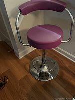 Single purple bar stool showing padded seat and backrest with chrome pedestal base on wood floor.