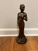 Full frontal view of the bronzed female statue showing the figure in a flowing dress with some surface wear and chips visible.