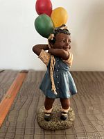 Front view of the figurine showing the girl holding balloons with smiling expression, in blue dress, standing on textured base.