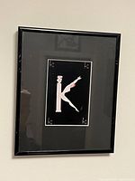 Framed Erte letter K artwork hanging on wall showing full frame and art detail.