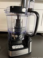Side view of food processor showing clear plastic bowl with handle and control panel buttons on black and stainless steel base