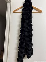 Full length of the black rabbit fur scarf hanging on a wooden hanger, showing the rich texture and cluster design of the fur.