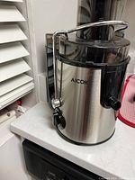 AICOK juicer placed on kitchen counter near window with white blinds.