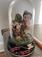 Front view of the Betty Boop jungle figurine under clear glass dome, showing Betty Boop and a small jungle explorer figure with details of foliage base.