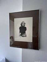 Framed black and white portrait drawing of Marilyn Monroe hanging on a wall, showing full framing and matting.