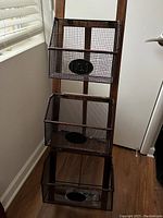 Full view of the three-tiered office stand with wire mesh baskets against a wall and window.