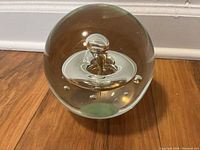 Clear glass spherical paperweight showing an internal water drop design with bubbles inside.
