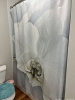 Photo of white fabric shower curtain with a large orchid flower printed on it, hanging on a shower rod with metal hooks attached.