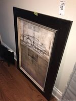 Full view of framed wall art leaning against a wall on wood floor, showing its size and frame style.