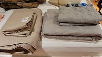 Two folded beige coverlets and grey coverlets neatly stacked on a bed, showing the overall lot contents.