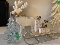 Full view of white wood reindeer, glass tree, and metal sled with gift boxes and tin tree