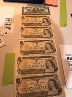 Photo showing six Canadian one dollar bills laid out, oldest printed 1939 with King George VI portrait and others with Queen Elizabeth II portraits.