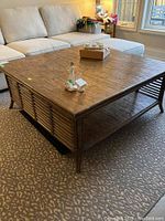 Full view of square wood and bamboo style coffee table placed in front of sofa, showing woven top surface and bamboo sides with slatted lower shelf.